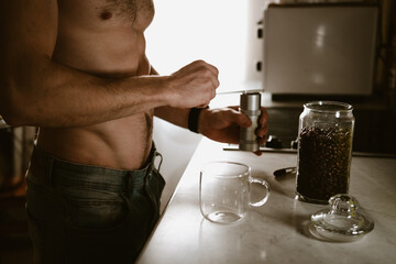 A naked man prepares coffee in the kitchen in the morning