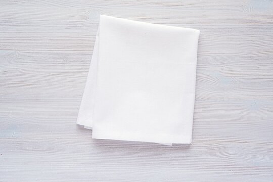 White plain fabric kitchen towel or tea towel folded on wooden background, mockup for design presentation.