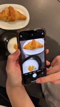 Women hands are filming coffee latte and croissant, filming on phone for social networks, preparing delicious food in cafe, sharing with friends, showing off, making vestments and posting stories.