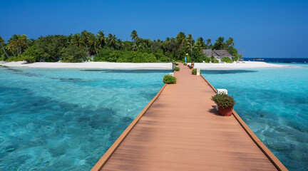 Wooden bridge over the sea leading to an island with sandy beaches and a green forest. Palm trees.