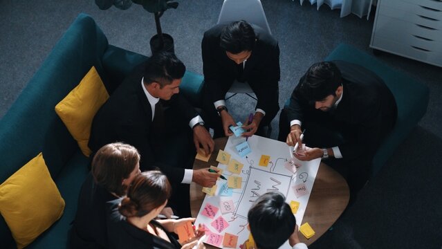 Top view of skilled businesswoman write marketing idea and placed sticky notes on mind mapping while planning financial strategy with diverse business group. Startup team working together. Directorate