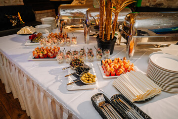 Riga, Latvia - January 18, 2024 - Catering buffet table with shrimp cocktails, salads in glasses, olives, plates, and food warmers.