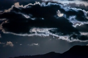 Luna piena coperta dalle nuvole con profilo di montagne