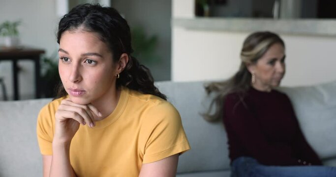 Silent teenage girl and mother sitting apart on sofa and not talking, thinking about problems, spoiled relationships, feel dissatisfied, resentment after quarrel. Disobedience, misbehavior, conflicts