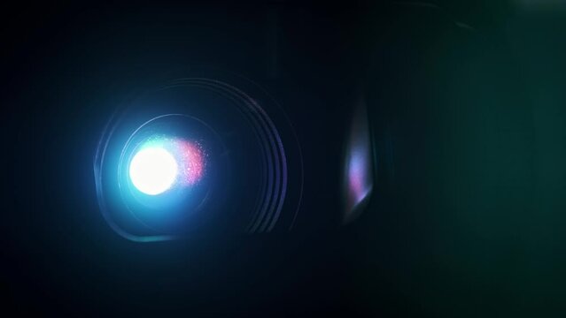 Multi-colored searchlight provides bright colored beam for broadcasting movies. Bright film projector with flashing rainbow lights close-up. Colored optical lens flare effect. Show slides, effect, FX.
