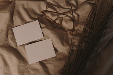 Paper sheets with blank copy space, glasses, dried grass on crumpled tan beige bed blanket with...