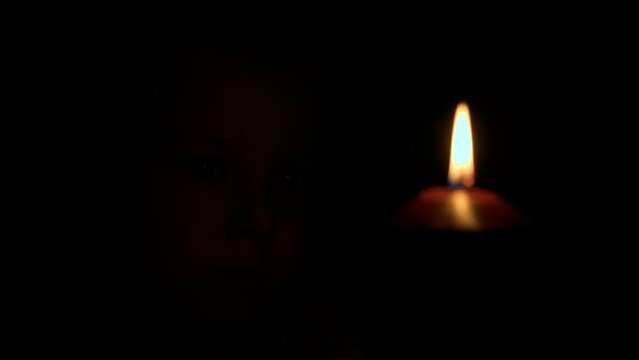 A child watches a burning candle, its flickering flame mirroring the pain in the young boy's eyes. The scene captures a moment of loss and suffering, as the child grapples with grief and sorrow.