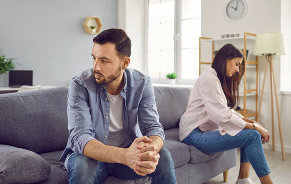 Disappointed couple sitting on sofa back to back, facing away from each other. Portrait of frustrated husband and wife feeling upset after argument and making decision of breaking up get divorced