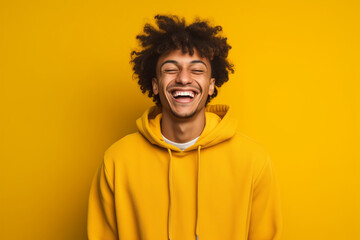 portrait of a man wearing a hoodie smiling in front of yellow background