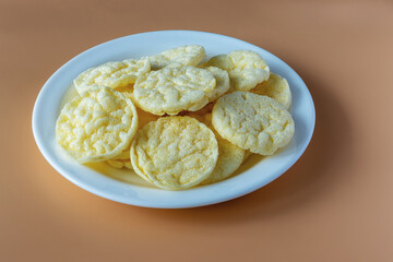 Round and crispy rice crackers on a white plate isolated on a beige background.
