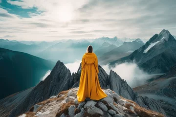 Fotobehang A person dressed in a yellow robe sits on top of a mountain, taking in the panoramic view. © pham