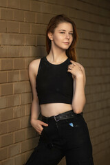Portrait of a young beautiful long-haired girl in dark clothes on a summer street.