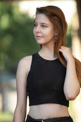 Portrait of a young beautiful long-haired girl in dark clothes on a summer street.