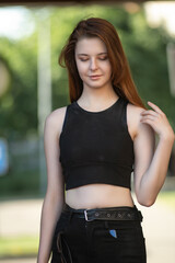 Portrait of a young beautiful long-haired girl in dark clothes on a summer street.