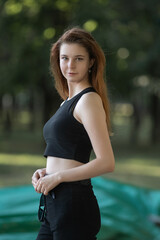 Portrait of a young beautiful long-haired girl in dark clothes on a summer street.