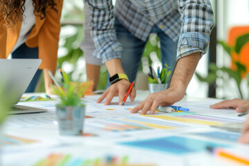 Fototapeta premium Close-up of a creative team's hands working together on colorful design plans spread across a table, with digital devices and stationery. 