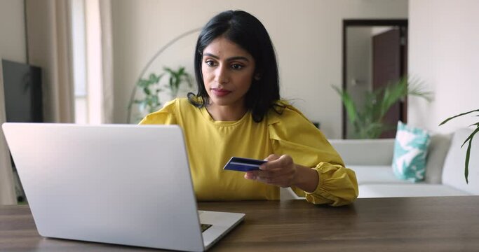 Young Indian woman sit at desk using laptop, try to make electronic payment by card, feels stressed, disappointed due to lack of money, extra fees for transaction, insecure payment, fraud and scams
