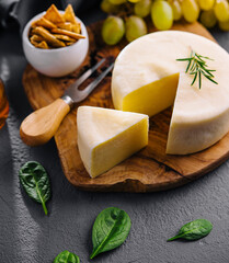 Round cheese on a wooden board and green grapes