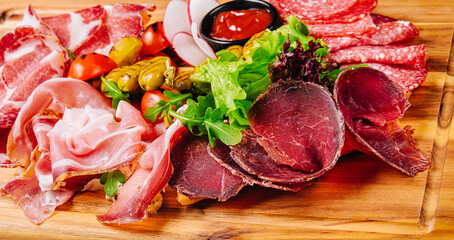 Variety of meats, sausages, salami, ham, olives, laid out on a wooden board