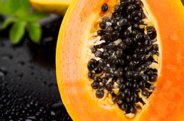 Papaya fruit on wet black background with water drops. Halved fresh organic Papaya exotic fruits with leaf close up. Healthy vegan food. Macro shot