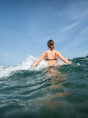 Fototapeta premium Joven en bañador entrando contenta al agua mientras las olas chocan contra su cuerpo, disfrutando del verano y el buen tiempo. Fotografía vertical