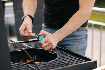 Close-up of human hand hold lighter and lights a fire in BBQ grill on terrace