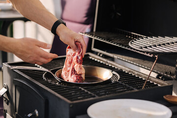 Male hand put T-bone Steak on a heated pan. Man grilling steak on carbon steel pan. French cuisine. BBQ concept