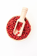 Red peppercorns in bowl with wooden scoop on white background. Dry white pepper grain