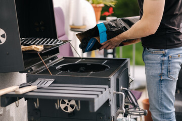 Close-up of man pours out charcoal into BBQ grill on terrace. Male preparing for backyard barbecue 