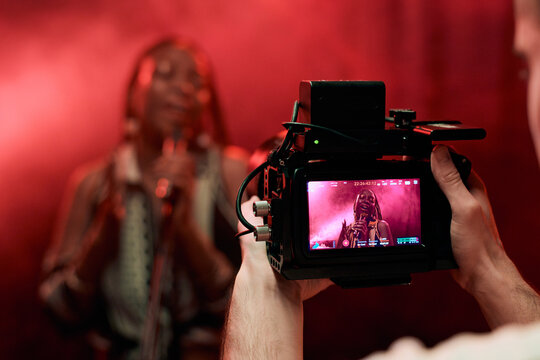 Close up of unrecognizable cameraman filming music video with focus on Black woman singing on camera screen copy space