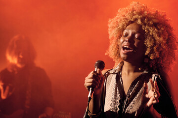 Waist up portrait of talented Black female musician singing to microphone during stage performance in nightclub copy space - obrazy, fototapety, plakaty