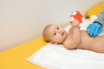 A pediatrician is examining the belly of a baby. A small child is playing with a toy while being...