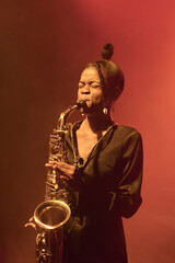 Vertical portrait of African American young woman playing saxophone while performing jazz music on...
