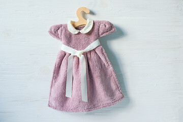 Girl's little dress made of terry cloth on a hanger. Flat lay top view on white wooden background.