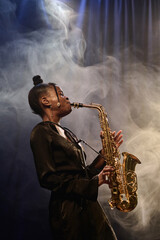 Vertical portrait of talented Black woman playing saxophone on stage during performance in jazz music club with smoke effect