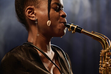Side view closeup of young Black female musician playing saxophone on stage with focus on jewelry
