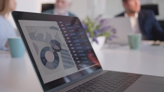 Company strategy analytics data on laptop screen in conference room close up selective focus. Business performance stats on computer with workers team talking in blurred background