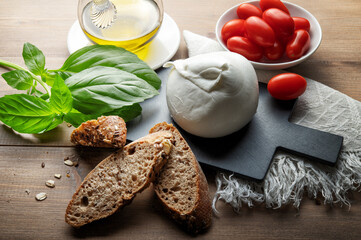 Buffalo mozzarella, cherry tomatoes, extra virgin olive oil and basil on wooden background, close-up.