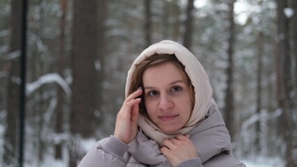 A young woman stands against a background of fir trees under a snowy forest in winter. A girl in a...