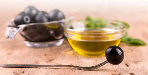 Olive oil with fresh herbs and olive on fork on the wooden background.on sunlight