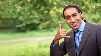 Handsome dark skin man making a call me sign and looking very happy in park