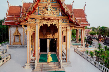 Travel by Asia. Young woman in hat and yellow dress walking near the Chalong buddhist temple on...