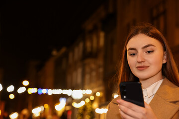 Beautiful woman using smartphone on night city street. Space for text
