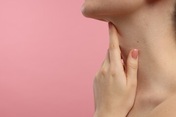 Woman touching her neck on pink background, closeup. Space for text