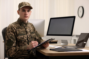 Fototapeta premium Military service. Young soldier with clipboard working at table in office