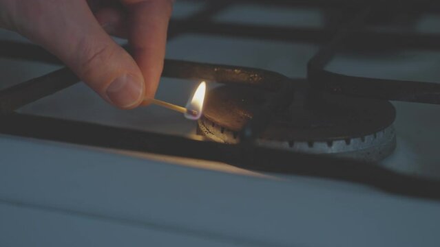 Man brings a lit match to a gas burner but the fire does not appear due to the lack of gas. The problem of the lack of natural gas in residential buildings due to shortage or high cost