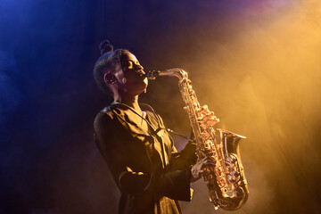 Portrait of passionate Black woman musician playing saxophone in jazz nightclub with golden hazy...
