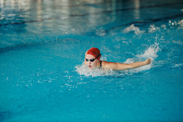 A professional female swimmer is swimming butterfly style in olympic pool.