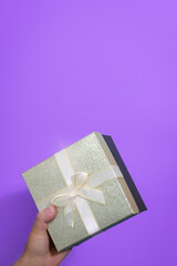Hand of a boy holding a classic gift box. Bow on the box. pink background. Close-up