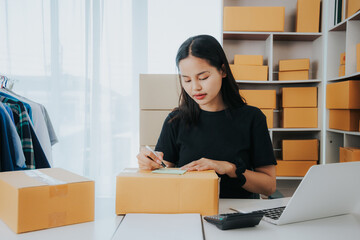 Asian small business owner working in home office with boxes, checking orders and preparing for delivery to customers. Online Marketing, SME Ecommerce Concepts